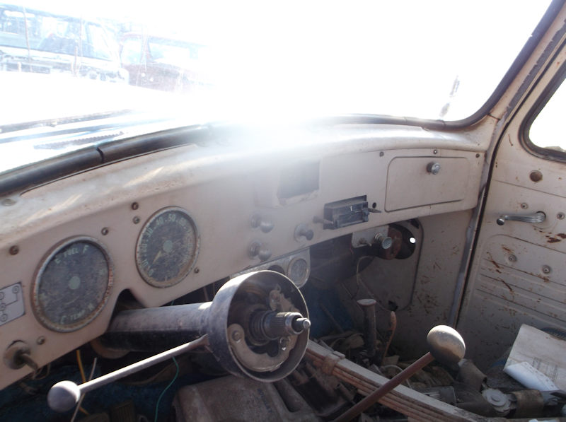 Interior view of a 1956 International Harvester truck showing the original grey metal dashboard, dual round gauge clusters, glove box, and steering column assembly.