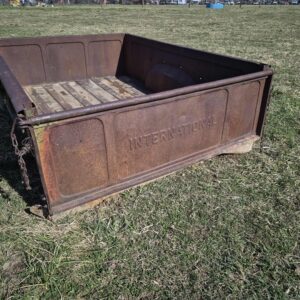 Vintage rusted International Harvester pickup truck step-side tailgate with stamped lettering sitting in a field